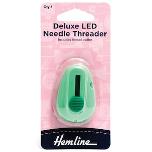 Op de afbeelding: Een mintgroene Deluxe LED-naaldinrijger met draadafsnijder, verpakt op een roze kaart met de tekst Qty 1, Deluxe LED Needle Threader, Includes thread cutter en Hemline. Het apparaat heeft een donkergroene schuifknop.