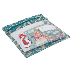 Pode incluir: Uma bolsa de zíper turquesa com estampa floral contendo um kit de ponto cruz. O kit inclui um pedaço de tecido Aida, fio e um padrão para uma cena de cabana de praia. O cartão do padrão diz "119 - Beach Huts 19 x 11"