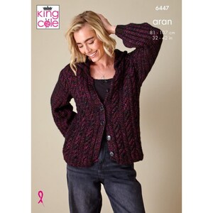 Può includere: Un cardigan lavorato a maglia Aran bordeaux con chiusura a bottoni. Il maglione ha un motivo strutturato e maniche lunghe. L'immagine include il testo "aran" e misure di 81-107 cm.