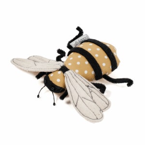 May include: A soft toy bee with a tan body, white polka dots, and black stripes. It has black antennae and eyes, and a tag that reads "hobby gifts". The wings are light grey.