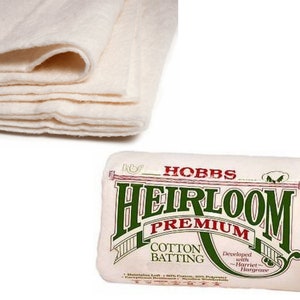 以下が含まれることがあります： 緑と赤のラベルが付いた白い綿の詰め物ロール。ラベルには「Hobbs Heirloom Premium Cotton Batting」と「Developed with Harriet Hargrave」と書かれています。