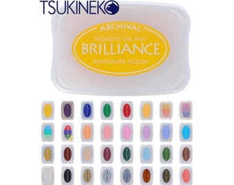 May include: A set of 48 archival pigment ink pads in various colours. The ink pads are labelled "Brilliance" and are arranged in a grid pattern. The ink pads are in a clear plastic container. The ink pads are made by Tsukineko.