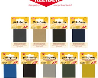 Può includere: Dieci confezioni di toppe termoadesive in vari colori, tra cui nero, marrone, verde scuro, grigio e oro. Ogni confezione riporta il testo "flick+fertig" e "Risse, Licher, dünne Stellen einfach zukleben" in tedesco. Le confezioni sono etichettate con la dimensione "25 x 5,8 cm" e "145 cm2".