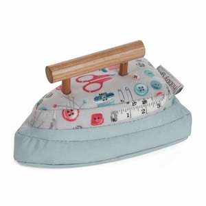 Peut inclure: Un coussin à épingles en forme de fer à repasser bleu clair avec une poignée en bois. Le coussin est décoré d'un imprimé sur le thème de la couture avec des boutons, des ciseaux, des aiguilles et un mètre ruban. Le texte "HOBBY" est visible sur le côté du coussin.