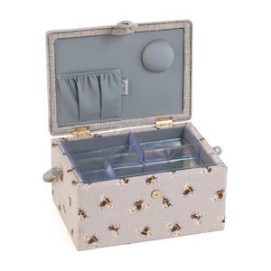 Puede incluir: Una caja de costura de tela gris con un patr&oacute;n de abejas. La caja tiene una bandeja de pl&aacute;stico transparente con divisores en el interior. La tapa tiene un forro de tela gris con un peque&ntilde;o bolsillo y un alfiletero.