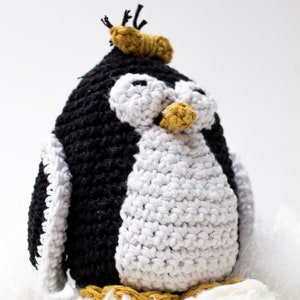 May include: A crocheted penguin toy with a black and white body and a yellow beak. The penguin is wearing a yellow crocheted hat.