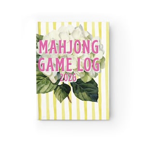 May include: A hardcover journal with a floral design and the text "MAHJONG GAME LOG 2026" in pink. The cover features a watercolor illustration of white hydrangea flowers and green leaves against a yellow and white striped background.