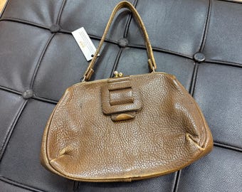 May include: A vintage brown leather handbag with a textured surface. The bag features a rectangular clasp and a short handle. The bag is sitting on a black leather surface.
