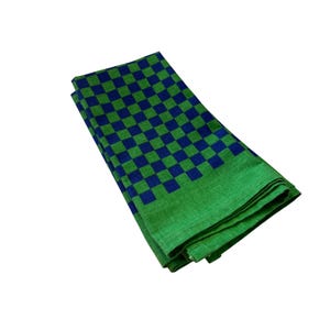 Op de afbeelding: Gevouwen groen en blauw geruite stof. De stof heeft een groene rand en een patroon van blauwe en groene vierkanten. De stof is gevouwen en lijkt van een zacht materiaal te zijn.