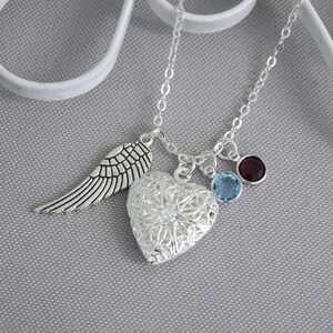 May include: Silver necklace with a heart locket, a single angel wing charm, and two small gemstone charms. The gemstones are blue and purple.