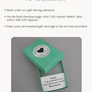 May include: A teal gift box with a white circular sticker featuring a black heart and the text Madie's Other Charms. Inside the box is a white card with the printed text: Emily, I'm so proud of you and I love you so much. Grandma.