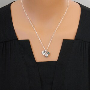 May include: A silver-toned chain necklace featuring a small circular charm engraved with the letter M, a miniature silver-toned volleyball charm, and a small, round, teal-colored accent bead hanging from the center of the delicate metal chain.