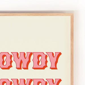 May include: A framed print with the text "Howdy" in pink and red letters on a cream background.