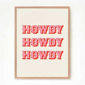May include: A framed print with the word "HOWDY" repeated three times in a pink and red retro font on a cream background.