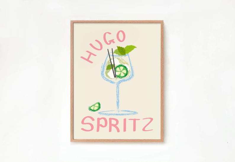 Op de afbeelding: Een ingelijst print met een lichte achtergrond met een handgetekende illustratie van een glas Hugo Spritz. De drank is afgebeeld met een lichtblauw glas, een groene limoenwig en een takje groene munt. De woorden "Hugo Spritz" zijn geschreven in roze cursief.