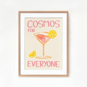May include: A framed print with a pink and yellow illustration of a cocktail glass with a lemon wedge. The text "Cosmos for Everyone" is written in pink.