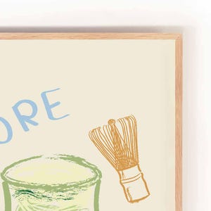 May include: A framed illustration of a glass of matcha with a whisk, with the word "MORE" written in blue letters on a cream background.