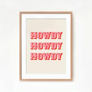 May include: A framed print with the word "HOWDY" repeated three times in a pink retro font on a cream background.