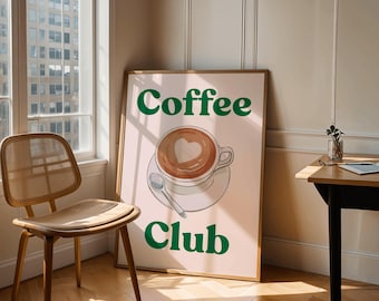 Puede incluir: Un póster enmarcado con las palabras "Coffee Club" en letras verdes. El póster presenta una taza de café con un diseño en forma de corazón en la espuma. Una silla y una mesa de madera están en primer plano.