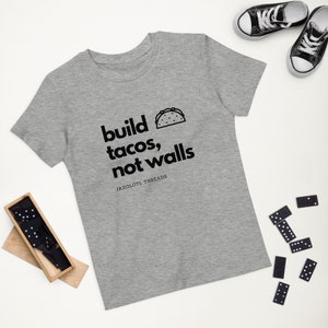 May include: A grey t-shirt with the text "build tacos, not walls" and a small black and white taco graphic. The text "JAXOLOTL THREADS" is printed below the graphic.