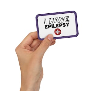 May include: A white card with a purple border and the text "I HAVE EPILEPSY" in black lettering. A red medical cross symbol is below the text.