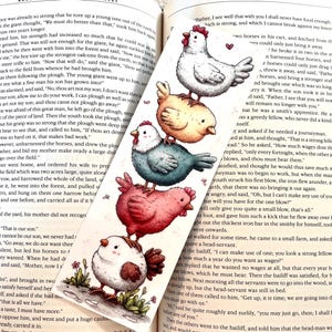 May include: A whimsical bookmark featuring a stack of illustrated chickens in white, yellow, teal, red, and white. The bookmark is set against an open book with text.
