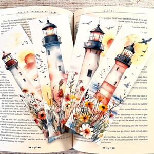 May include: Set of four watercolor lighthouse bookmarks with floral accents. Each bookmark features a different lighthouse design with a sunset or sunrise backdrop, and flying birds. The bookmarks are displayed inside an open book.