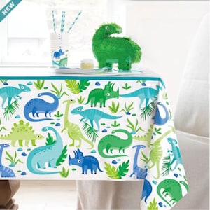 May include: A white tablecloth with a blue border features a dinosaur theme. The tablecloth is decorated with green, blue, and light blue dinosaurs on a white background. The tablecloth is perfect for a dinosaur-themed party.