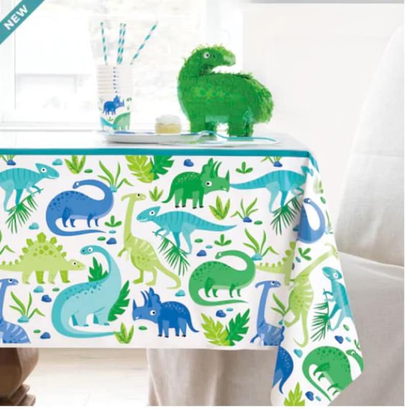 May include: A white tablecloth with a blue border features a dinosaur theme. The tablecloth is decorated with green, blue, and light blue dinosaurs on a white background. The tablecloth is perfect for a dinosaur-themed party.