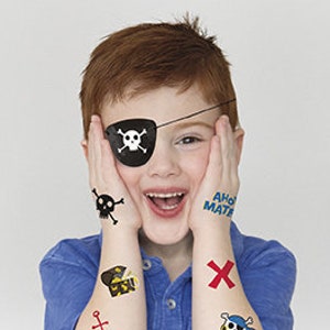 May include: A young boy wearing a pirate costume with a black eye patch, a skull and crossbones tattoo, and other pirate-themed tattoos on his arms. The tattoos include a treasure chest, an anchor, and a skull and crossbones.