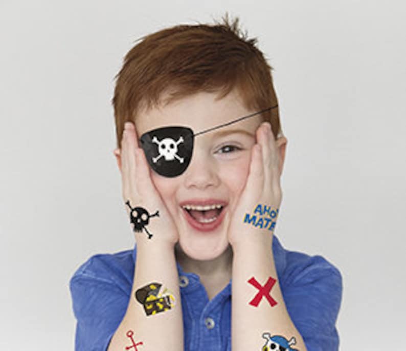 May include: A young boy wearing a pirate costume with a black eye patch, a skull and crossbones tattoo, and other pirate-themed tattoos on his arms. The tattoos include a treasure chest, an anchor, and a skull and crossbones.