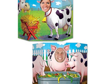 Könnte beinhalten: Zwei Fotokabinen-Requisiten zum Thema Bauernhoftiere. Eines zeigt eine Kuh mit einer Glocke und dem Gesicht einer Person im Ausschnitt. Die andere Requisite hat Schweine um einen Trog.