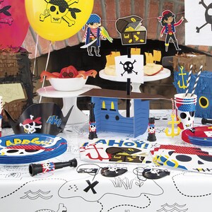 May include: A pirate-themed party table setting with blue and red plates, cups, and napkins featuring skull and crossbones designs. There are also pirate hats, a telescope, and a small blue ship with a skull and crossbones flag.