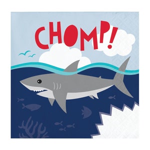 May include: A square paper napkin with a cartoon shark design. The shark is gray with white teeth, swimming in blue water. The word "CHOMP!" is written in red above the shark, with white clouds and blue sky in the background.