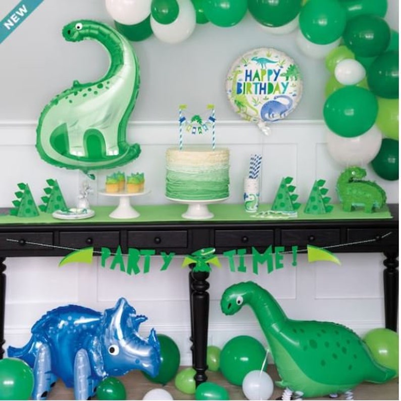 May include: A green and white dinosaur party theme with a green and white ombre cake, green and white balloons, and a green and white dinosaur balloon. The table is decorated with green and white paper plates and napkins. The banner says "Party Time!"