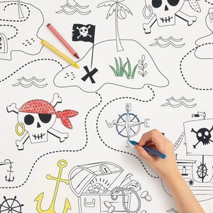 May include: A black and white pirate treasure map with a compass, skull and crossbones, a treasure chest, and anchors. A hand is coloring the map with blue, red, and yellow crayons.