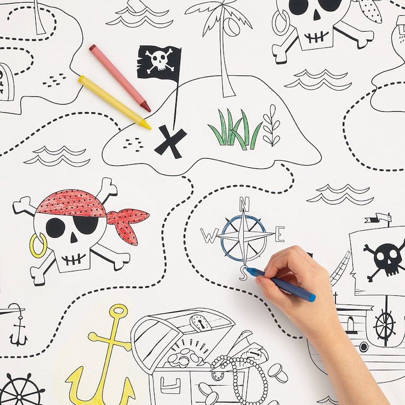 May include: A black and white pirate treasure map with a compass, skull and crossbones, a treasure chest, and anchors. A hand is coloring the map with blue, red, and yellow crayons.