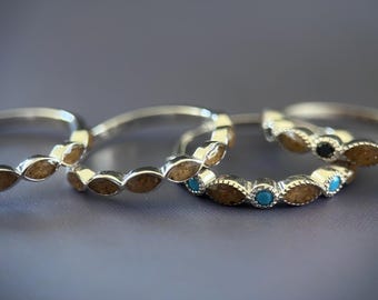 May include: Four silver hoop earrings with decorative oval-shaped accents. The earrings feature brown, turquoise, and black stones. The earrings are displayed on a grey surface.
