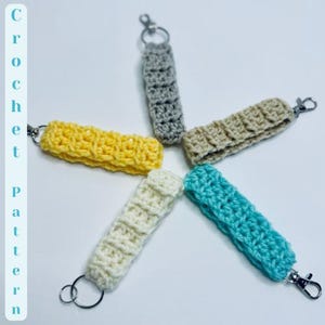 May include: Five crocheted keychains in different colors, including yellow, white, gray, beige, and turquoise. Each keychain has a silver key ring.
