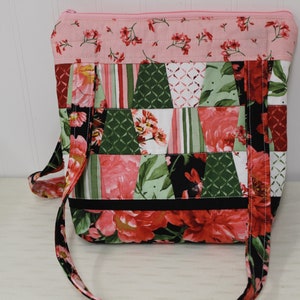 May include: A patchwork tote bag with a floral print in shades of pink, green, black, and white. The bag has a long strap and a zipper closure.