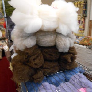 May include: A collection of brown, white, and beige wool fibers arranged in a decorative display. The fibers are fluffy and soft, and they are arranged in a way that suggests a human figure. The fibers are displayed on a metal rack.