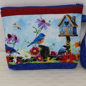 May include: Blue zippered pouch with a blue bird, a birdhouse, and flowers on a blue and white background. The pouch has a red and blue trim and a blue handle.
