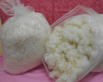 May include: Two clear plastic bags filled with white fluffy stuffing. The bags are on a pink surface.
