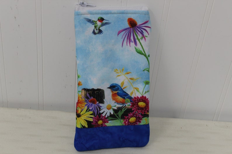 May include: A blue zippered pouch with a floral print featuring a hummingbird, a bluebird, and various flowers. The pouch has a blue fabric lining.