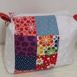 May include: A white zippered pouch with a patchwork design. The patchwork is made of different fabrics with floral and geometric patterns in red, blue, purple, green, and yellow.