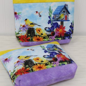 May include: Two small zippered pouches with a floral and bird print. The pouches are lined with purple fabric and have a yellow trim. The print features a birdhouse, birds, and flowers.
