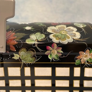 May include: Black mailbox with a gold trim and a white flag. The mailbox is decorated with hand-painted flowers in shades of pink, white, and green.
