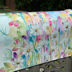 May include: A white mailbox with a hand-painted design of white daisies and colourful flowers on a blue background.