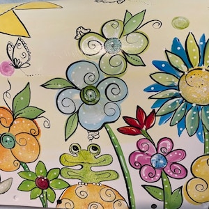 May include: A hand-painted mailbox with a whimsical design featuring a frog, flowers, butterflies, and a sun. The flowers are in shades of blue, yellow, pink, and green. The mailbox is painted on a white background.