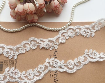 May include: White lace trim with a delicate floral pattern. The lace is approximately 2.5 cm wide and has a scalloped edge.
